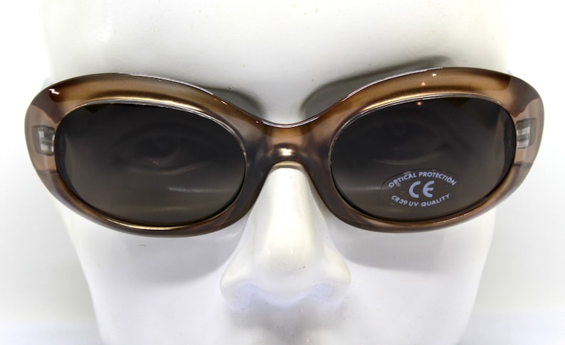 May include: Brown oval-shaped sunglasses with dark lenses. The sunglasses have a CE mark and the text "Optical Protection CE 3.1 UV Quality" on the right lens.