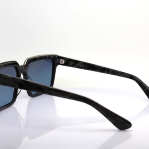 May include: Black square sunglasses with a dark blue lens and a black and silver frame. The frame has a marbled pattern.