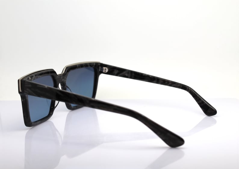 May include: Black square sunglasses with a dark blue lens and a black and silver frame. The frame has a marbled pattern.