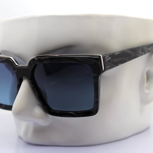 May include: Black square sunglasses with a marble pattern on the frame and dark blue lenses.