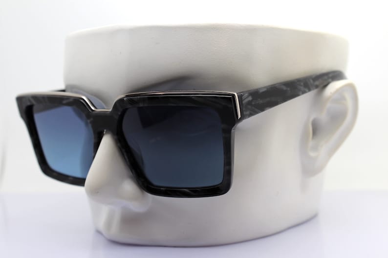 May include: Black square sunglasses with a marble pattern on the frame and dark blue lenses.