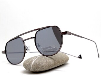 May include: Brown metal aviator sunglasses with dark gray lenses. The sunglasses are resting on a gray rock. The brand name "elevenparis" is visible on the lenses.