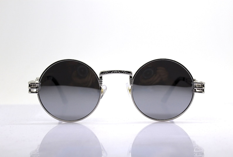 K&ouml;nnte beinhalten: Silberne runde Sonnenbrille mit dunkelgrauen Gl&auml;sern. Die Sonnenbrille hat einen detaillierten Metallrahmen.