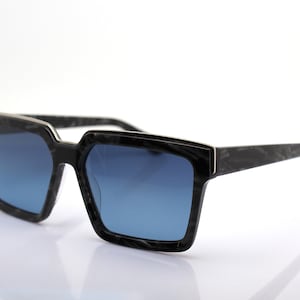 May include: Black square-shaped sunglasses with blue lenses and a black and silver frame.