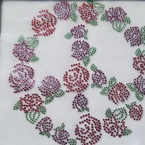May include: A white fabric background with a design of pink, red, and purple rhinestones arranged in the shape of a circle of roses.