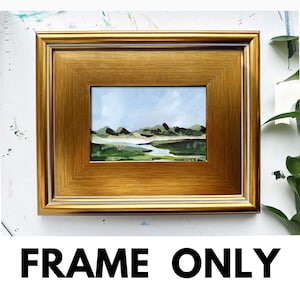 May include: A gold-colored picture frame with a white inner border. The frame is empty and ready to display a painting or photograph.