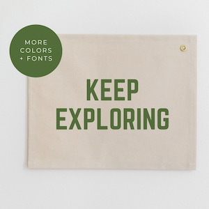 May include: A beige canvas wall tapestry with the text "KEEP EXPLORING" printed in dark green.