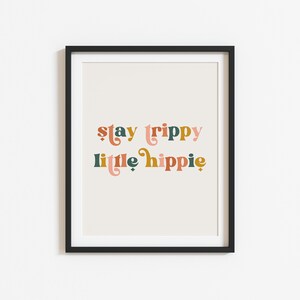 Pode incluir: Uma impress&atilde;o emoldurada com o texto "stay trippy little hippie" em uma fonte retr&ocirc;. O texto est&aacute; em tons de rosa, laranja, verde e marrom.