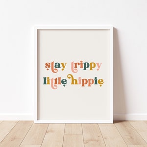 Pode incluir: Uma impress&atilde;o emoldurada branca com o texto "stay trippy little hippie" em letras estilizadas coloridas.