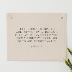 May include: A beige canvas wall tapestry with the text "LET THE MORNING BRING ME WORD OF YOUR UNFAILING LOVE, FOR I HAVE PUT MY TRUST IN YOU. SHOW ME THE WAY I SHOULD GO, FOR TO YOU I ENTRUST MY LIFE. psalm 143:8"