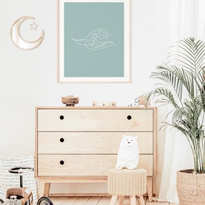 May include: A framed print with a minimalist white wave design on a teal background. The artwork is displayed above a wooden chest of drawers. A crescent moon mirror and a white bear figurine are also visible.