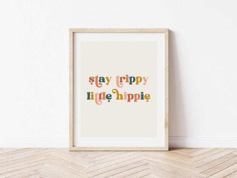 Pode incluir: Uma impress&atilde;o emoldurada com o texto "stay trippy little hippie" em um estilo de fonte retr&ocirc;. O texto est&aacute; em tons de rosa, verde e laranja sobre um fundo bege.