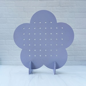 Puede incluir: Un soporte para pendientes de color lavanda en forma de flor con un soporte. El soporte tiene muchos agujeros pequeños para guardar los pendientes.