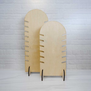 May include: Two wooden jewelry display stands with rounded tops and multiple slots for holding necklaces or bracelets. The stands are made of light brown wood and have a natural finish.