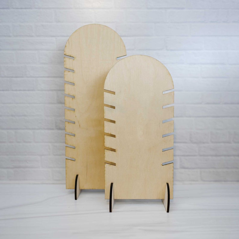 May include: Two wooden jewelry display stands with rounded tops and multiple slots for holding necklaces or bracelets. The stands are made of light brown wood and have a natural finish.