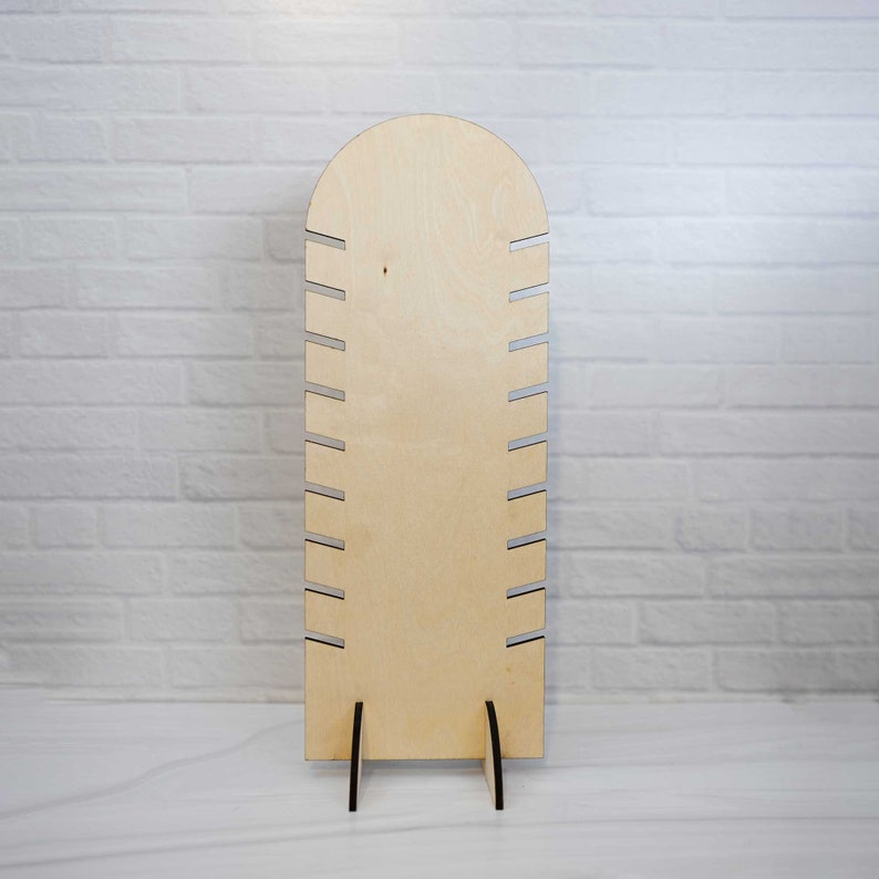 May include: A wooden jewelry stand with a rounded top and a stand with three legs. The stand has 10 slots for holding necklaces or bracelets.