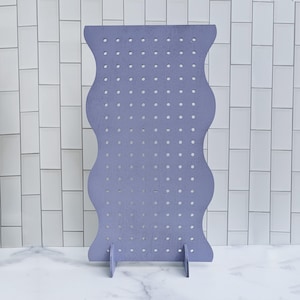 May include: A purple earring display stand with a wavy design and multiple holes for hanging earrings.