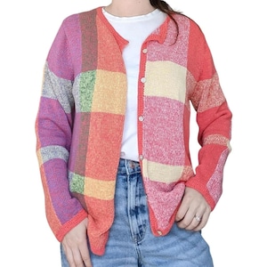 May include: A long-sleeved knit cardigan featuring a multi-colored plaid pattern in shades of pink, orange, yellow, green, and purple. The garment has a round neckline, a button-down front with small white buttons, and a ribbed trim along the edges.