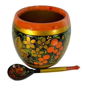 May include: A hand-painted wooden bowl and spoon set. The bowl is round with a black background, gold trim, and orange and yellow floral designs. The spoon has a black handle and a gold stem with red and orange floral details.