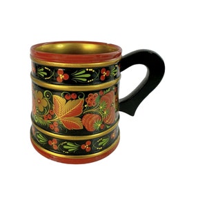 May include: A black wooden mug with a red, gold, and green floral design. The mug has a black handle.