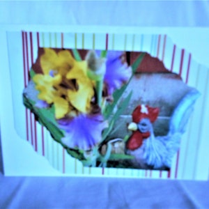 May include: A greeting card with a colorful striped background and a cutout window showing a rooster figurine and yellow and purple flowers.
