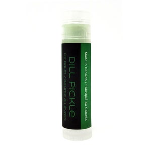 Könnte beinhalten: Ein grünes und schwarzes Lippenbalsam-Röhrchen mit dem Text "DILL PICKLE" und "LIP BALM / BAUME À LÈVRES" auf dem Etikett. Das Etikett trägt außerdem den Hinweis "Made in Canada / Fabriqué au Canada".