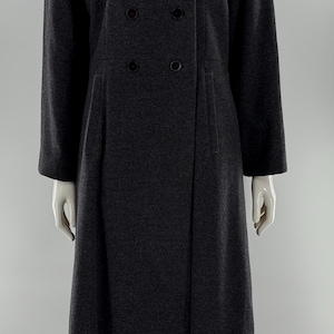 May include: A long, dark charcoal gray double-breasted coat featuring a wide notched collar, long sleeves, and four visible black buttons arranged in two vertical rows on the front. The coat has a structured fit with a straight hemline.