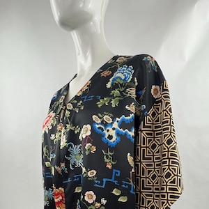 Puede incluir: Bata negra estilo kimono con cuello en V y mangas hasta el codo. La bata presenta un estampado floral y de pájaros en tonos rojos, azules y verdes. Una manga tiene un patrón geométrico dorado. La bata se exhibe en un maniquí.
