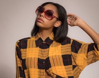May include: A woman wearing a yellow and black plaid shirt with a yellow suede shorts with lace-up detail.