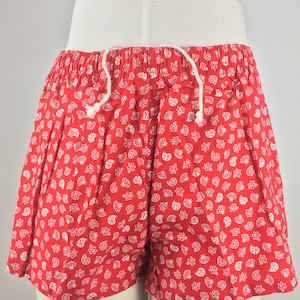 May include: Red shorts with a white seashell pattern. The shorts have a drawstring waist.