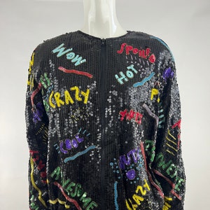 May include: A black sequined jacket with a zipper closure. The jacket is covered in colorful embroidered words and phrases, including "Wow", "Crazy", "Cool", "Awesome", "Spoiled", "Hot", "Yume", "Love", "Jaz", and "Invite".