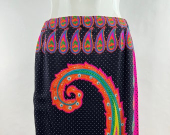 May include: A long, black skirt with a vibrant paisley design in orange, pink, and teal. The skirt features a white polka dot pattern and a bright pink border. The waistband has a repeating paisley pattern in pink, orange, and green.