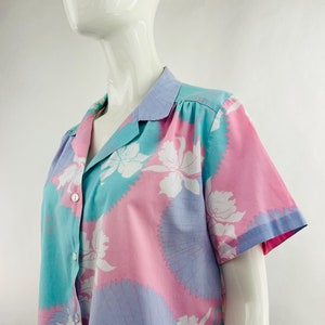 May include: A short-sleeved button-down shirt with a floral pattern. The shirt features a pastel color scheme of pink, blue, and turquoise, with white floral designs. The collar and cuffs are trimmed in blue.