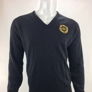 Puede incluir: Un suéter negro de cuello en V con un logotipo bordado en oro que dice "The Virginia Military Institute" y "VMI" en un círculo.