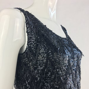 May include: A black sleeveless top with a sequined and fringed design. The sequins are small and closely spaced, creating a shimmering effect. The fringe is made of thin strands of fabric that hang down from the sequins.