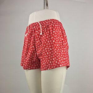 May include: Red shorts with a white floral print. The shorts have a drawstring waist.