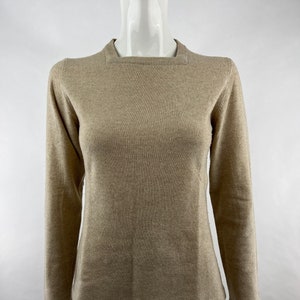 May include: A beige long-sleeved sweater with a round neckline.