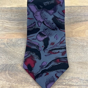 May include: A gray silk tie with a pattern of abstract shapes in shades of purple, red, and black.