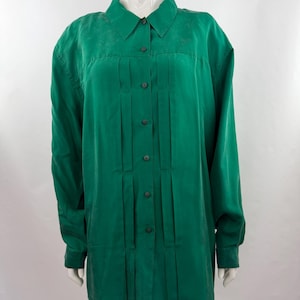 May include: A long-sleeve button-down shirt in a vibrant emerald green color. The shirt features a classic collar, a front button placket, and vertical pleat detailing running down the center of the chest. The fabric has a subtle sheen.