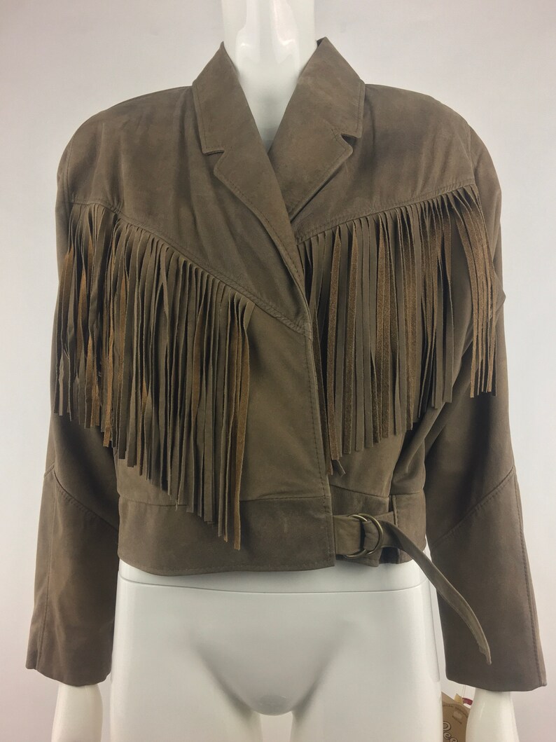 May include: A brown suede jacket with fringe detailing around the collar and hem. The jacket has a belt with a metal buckle.