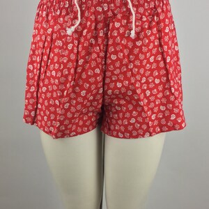 May include: Red shorts with a white seashell pattern. The shorts have a drawstring waist.