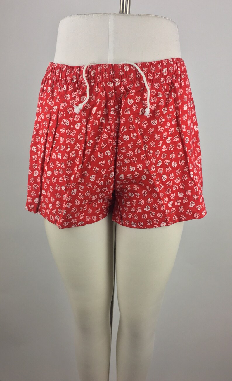 May include: Red shorts with a white seashell pattern. The shorts have a drawstring waist.