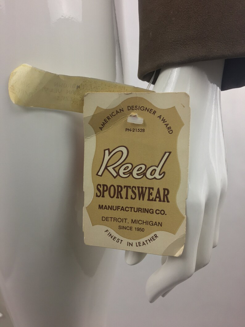 May include: A brown leather tag with the text "American Designer Award" and "Reed Sportswear Manufacturing Co. Detroit, Michigan Since 1950 Finest in Leather".