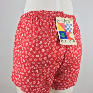 May include: Red and white patterned shorts with a white label that says "NEWPORT BLUE" with a nautical design.
