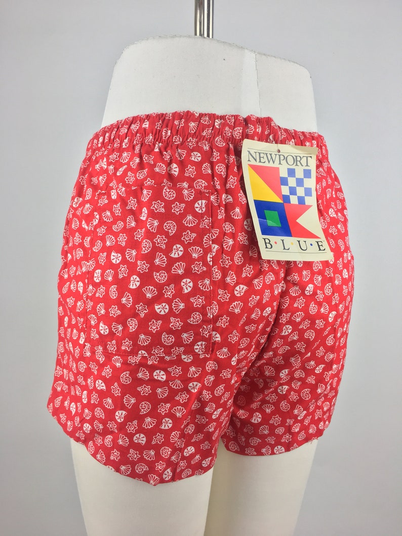 May include: Red and white patterned shorts with a white label that says "NEWPORT BLUE" with a nautical design.