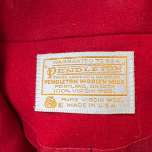 May include: Close-up of a bright red garment with a white label. The label reads "PENDLETON WOOLEN MILLS, PORTLAND, OREGON, 100% VIRGIN WOOL, PURE VIRGIN WOOL, MADE IN U.S.A."