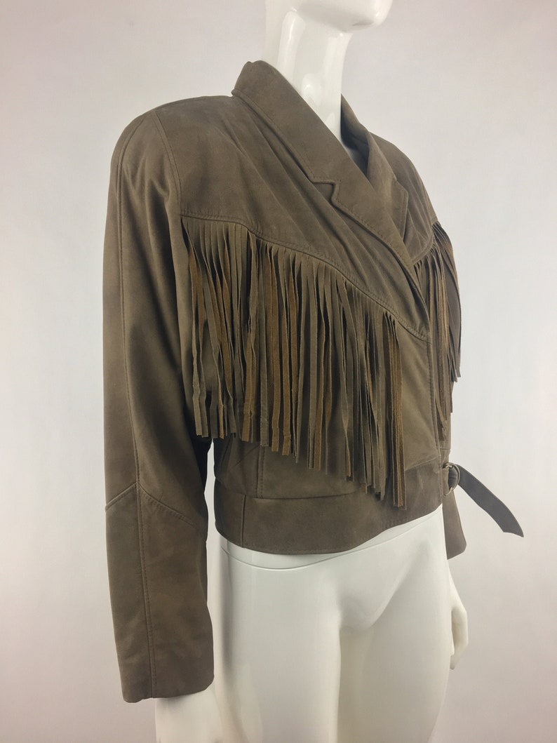 May include: A brown leather jacket with fringe detailing. The jacket has a  collar and a belt.