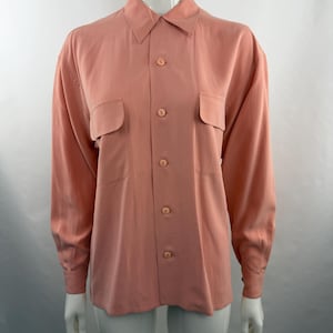 May include: A long-sleeved button-down shirt in a solid dusty rose color. The shirt features a classic collar, two chest pockets with flaps, and matching round buttons down the front placket and on the cuffs of the sleeves.