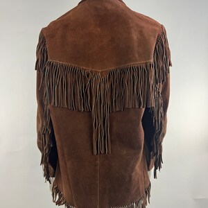 May include: Brown suede jacket with fringe detailing on the front, sleeves, and hem.