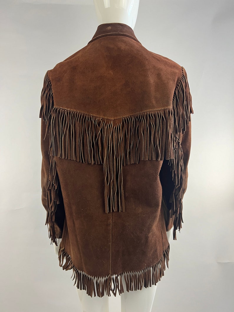 May include: Brown suede jacket with fringe detailing on the front, sleeves, and hem.